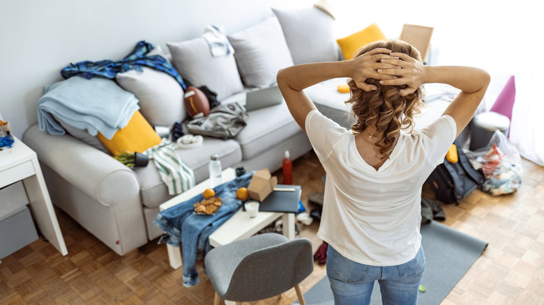 woman with hands on head looking at a messy living room