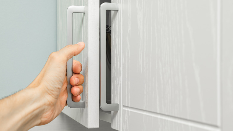 a man's hand grabbing a cabinet handle