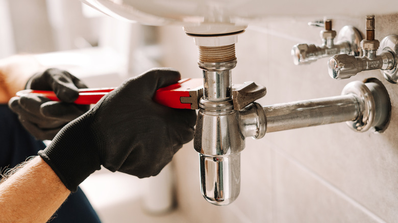 A person wearing black gloves using a wrench to tighten metal plumbing.