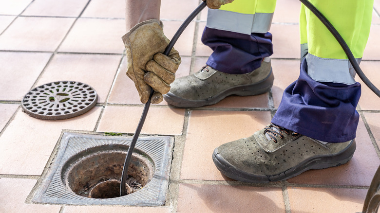 A person pushing a snake through a cleanout in a tiled floor