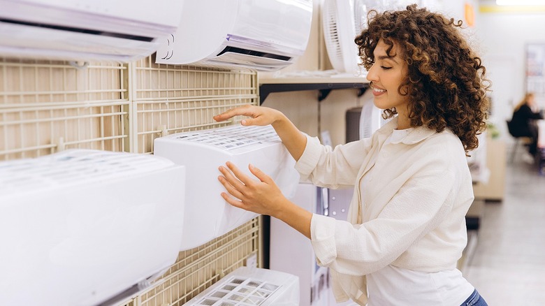 A person smiles while checking out different types of wall AC units in a store
