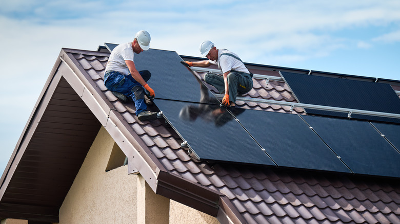 Workers install solar panels on a tile roof.