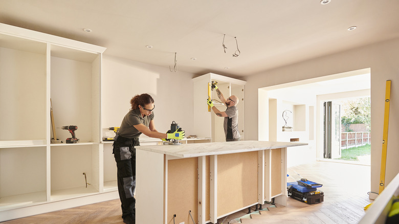 Two men installing cabinets in a room that opens to a yard