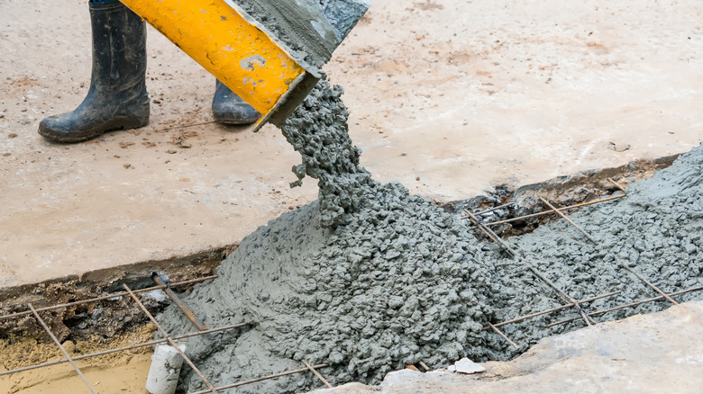 Wet concrete being poured into a trench with metal grid.