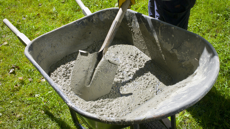 Someone mixing DIY concrete in a wheelbarrow with a shovel.