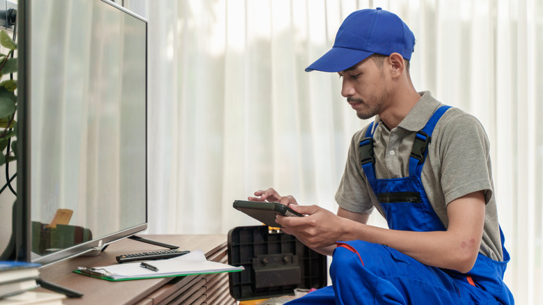 A worker in blue overalls repairing a flat screen television
