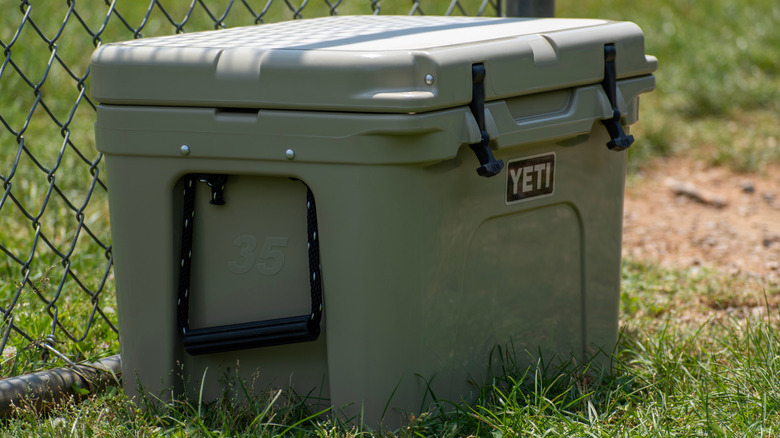 Green Yeti cooler sitting in the grass beside a black chain link fence.