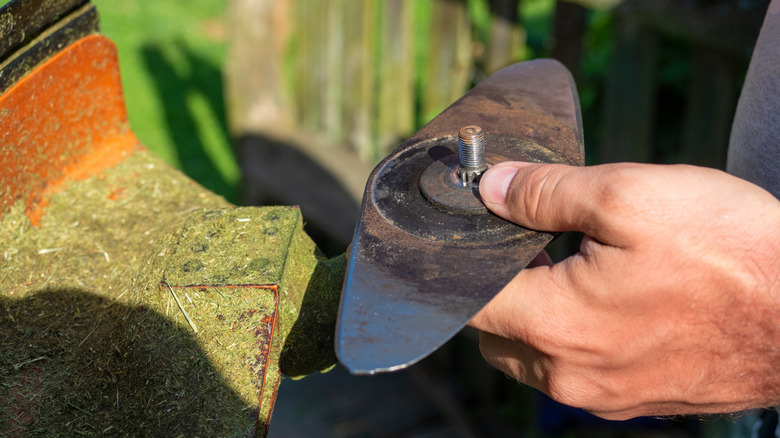 A person holding the removed blade from a lawn mower