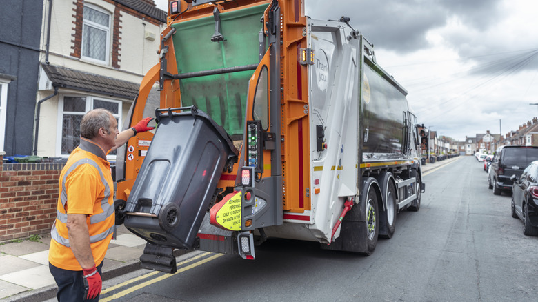 A garbage truck using the stop bar to lift and dump a bin of trash into the back.