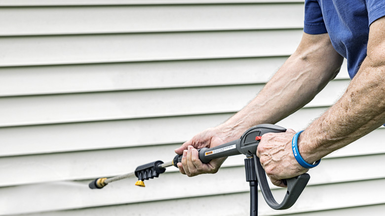 A person holding a pressure washer while cleaning vinyl siding on a house.