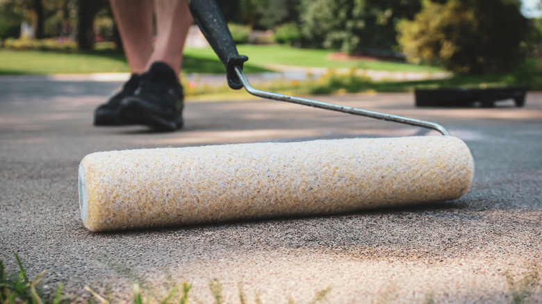 A person using a roller to seal a concrete driveway