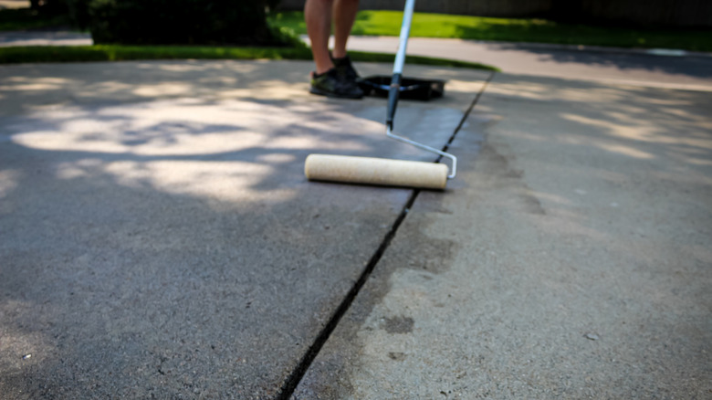 A person sealing a concrete driveway with a roller