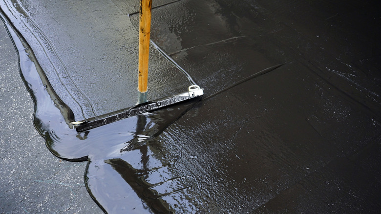 A person sealcoating an asphalt driveway with a squeegee