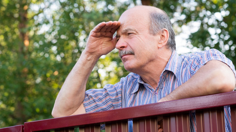 A neighbor man looking over the fence while shielding his eyes from the sun.