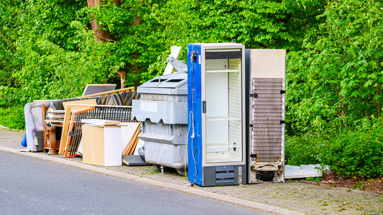 A trash site with a blue refrigerator without a door.