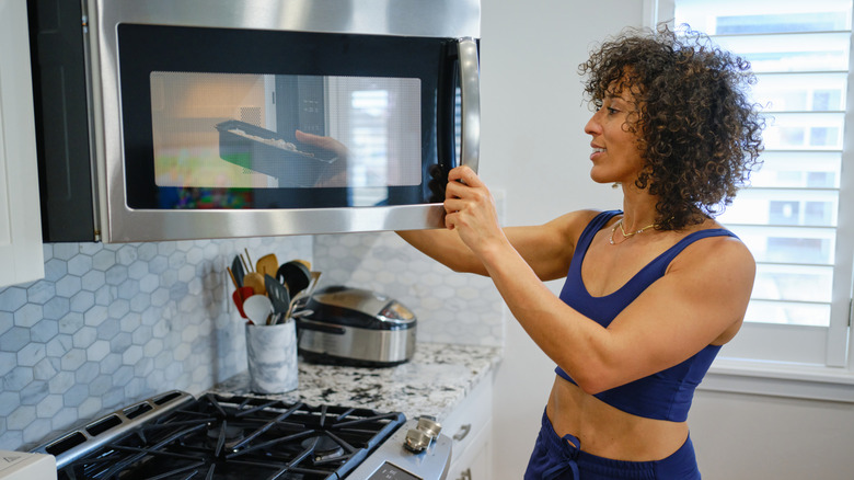 Woman in athletic wear putting food in an over the range microwave.