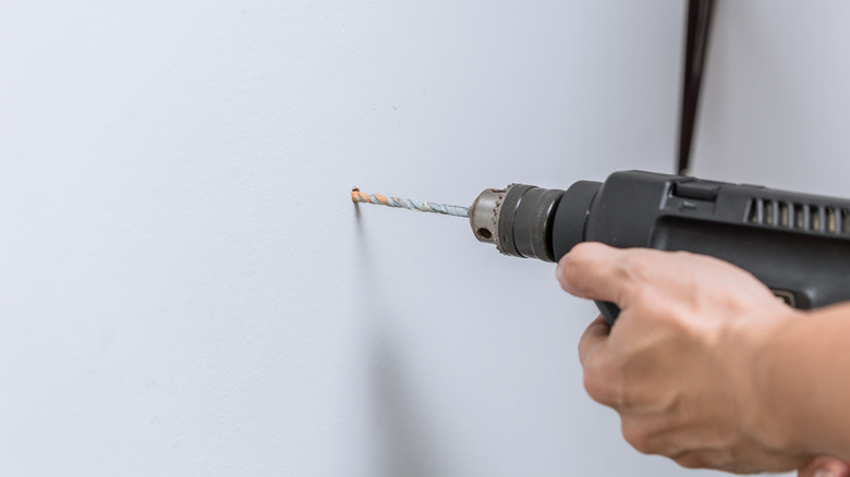 A closeup of hand drilling hole in the wall