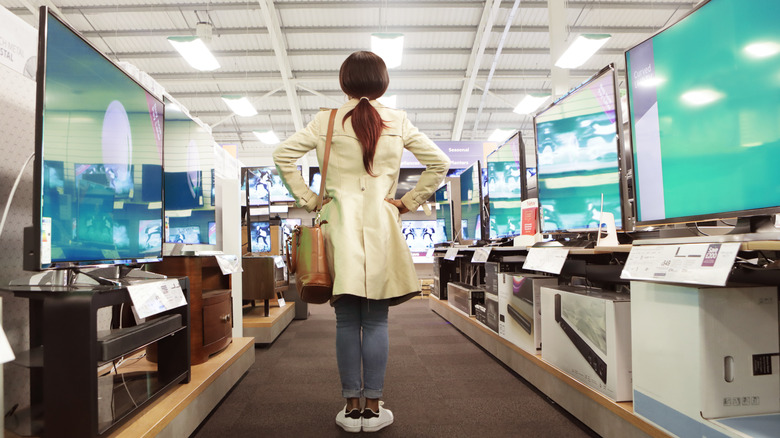 A person stands in the middle of an aisle with different TV displays on either side