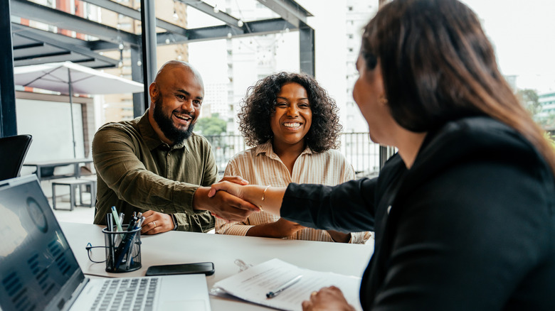 A man and a woman shaking hands with someone while sitting inside an office