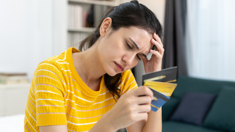 A woman holding three credit cards while looking tired or defeated