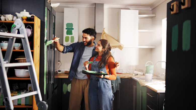 A couple painting kitchen cabinets green.
