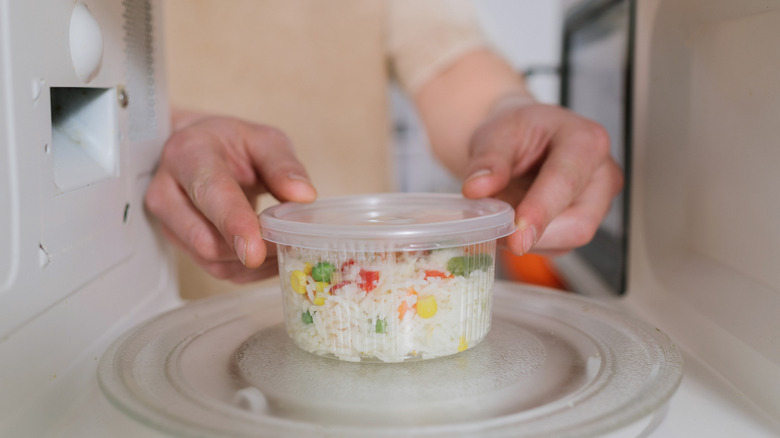 Person putting a clear container of leftover rice and vegetables inside a microwave