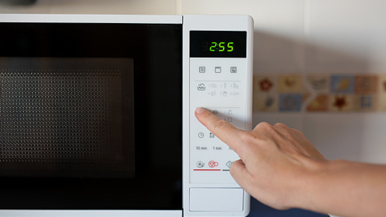 Hand pressing button on a white microwave with the timer set to 2:55