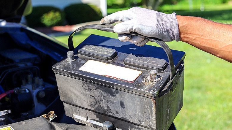 Close-up of a person's gloved hand holding a used lead-acid battery