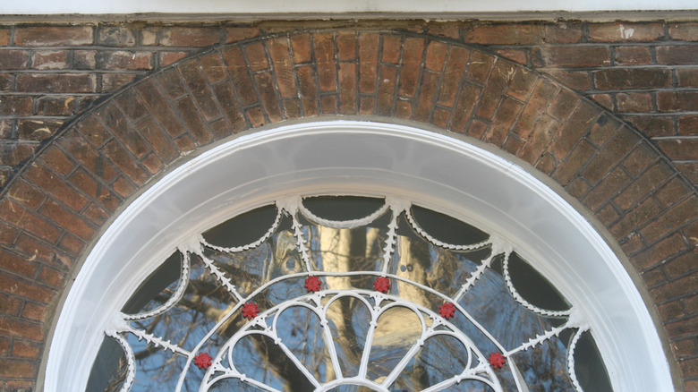 Arched stained glass window above door in brick wall.