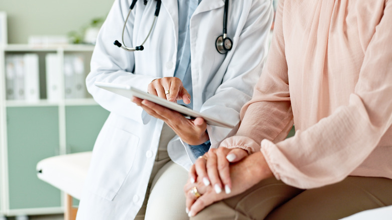 Hands of a doctor showing a patient information on a tablet