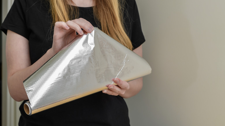 A person unrolling a roll of aluminum foil