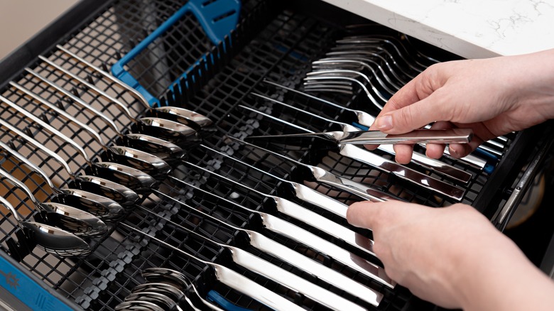 Person loading cutlery into dishwasher