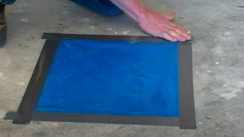 A person taping a piece of plastic to concrete