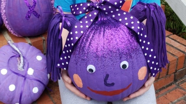 Girl holding purple-painted pumpkin