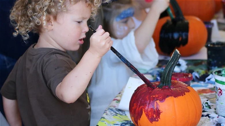 child paints pumpkin red