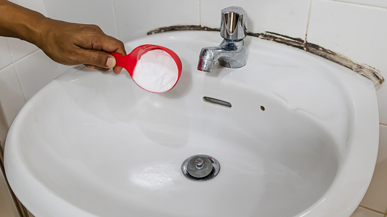 Person pouring baking soda down bathroom sink drain