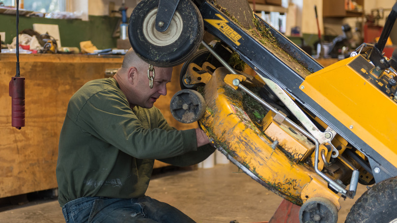 Man fixing a riding lawn mower deck and blades