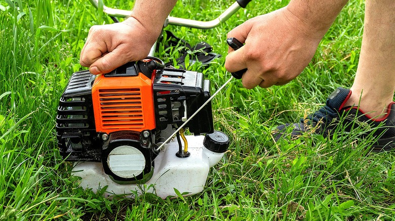 Close-up of a person pulling the starter cord of a small engine attached to a lawn mower
