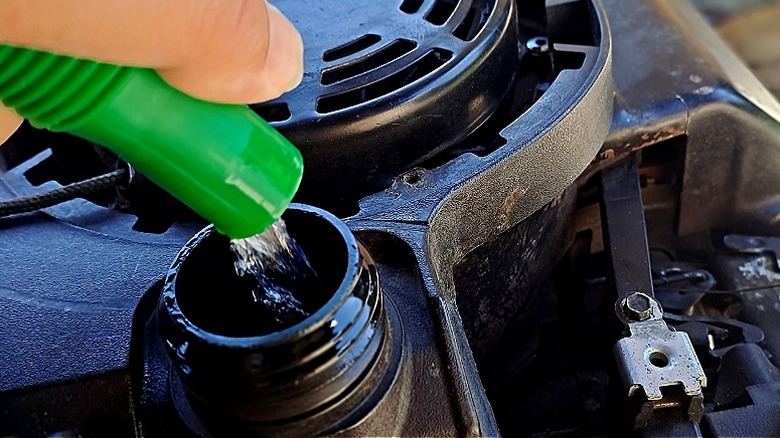 Close-up of pouring engine oil into a lawn mower engine during routine maintenance.