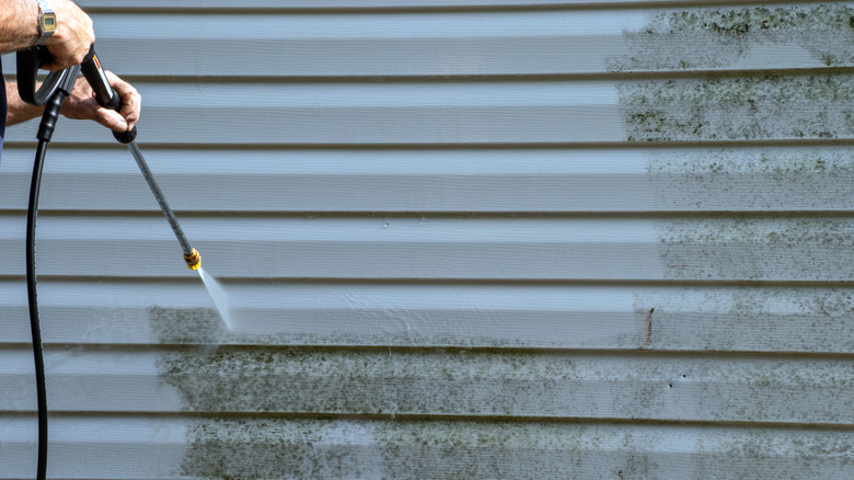 Man with large wristwatch power washing vinyl siding of mold and mildew