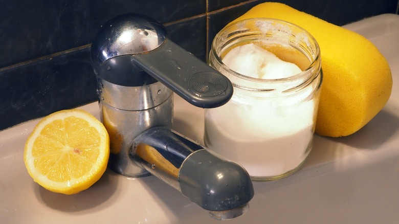 A jar of baking soda, a sliced lemon, and a sponge on bathroom sink