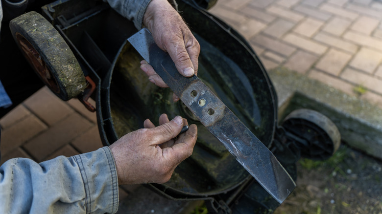A man holding a lawn mower blade and a bolt in his hands