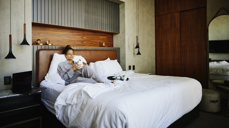 Woman in hotel room laying in bed with room service
