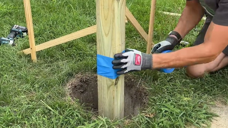Man applying painter's tape to a wood fence post