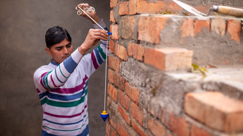 person checking if a wall is plumb with plumb bob