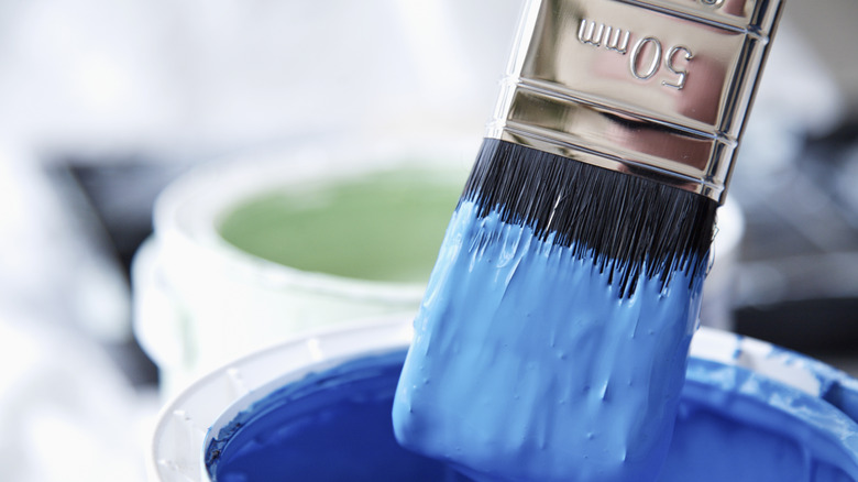 A wet paintbrush dripping with blue paint over a can