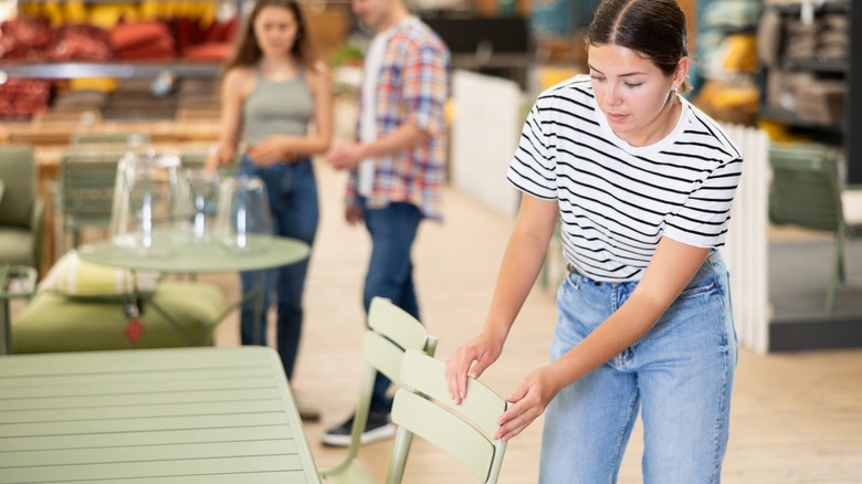 A woman browsing patio furniture in a showroom or store, her hand on a light green chair patio chair