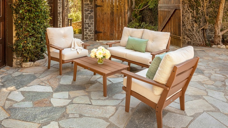 Set of brown POLYWOOD furniture with two chairs and a love seat on a stone patio with brown doors, a set of yellow daisies on the table