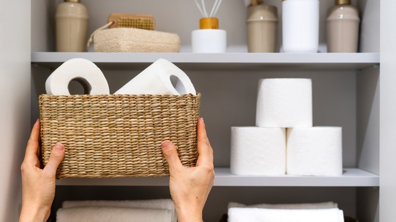 Restocking a wicker basket of toilet paper in a bathroom cabinet.