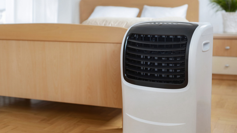 A portable air conditioner in front of a wooden bed